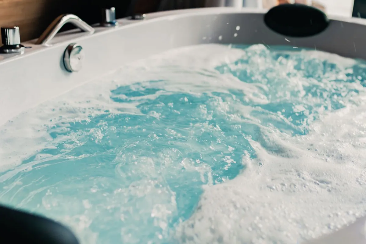 Clear blue water bubbling in an indoor hotel hot tub with the jets running and the control dials visible on the rim
